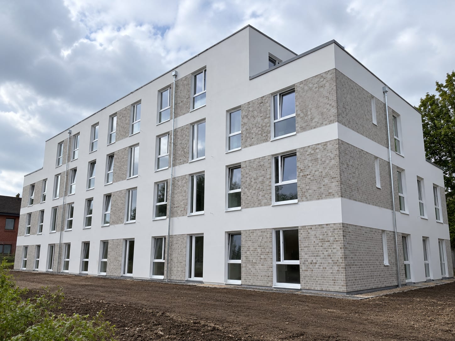 Dasselbe Mehrfamilienhaus mit fertiger heller Putzfassade und Klinkerriemchen-Flächen